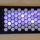 Černý MIDI kontrolér s mřížkou podsvícených hexagonálních polí. Na levé straně jsou čtyři otočné knoflíky a nápisy INTUITIVE INSTRUMENTS, EXQUIS, USB…