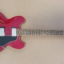 Červená polodublová elektrická kytara s černým pickguardem a bílými snímači. Na hlavě hmatníku je bílý nápis Epiphone a logo ve tvaru listu. Nástroj…