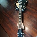 Černá elektrická kytara s bílým pickguardem a dvěma humbuckery. Na hlavě hmatníku je bílý nápis greco a pod ním v oválném rámečku nápis Standard. Nás…