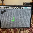 Kytarový kombozesilovač s černým krytím a stříbrnou textilní maskou. Na ovládacím panelu jsou nápisy CUSTOM, VINTAGE a VIBROLUX REVERB-AMP, dále ozna…