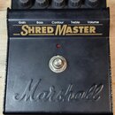 Černý kytarový efekt pedál s pětiknobovými ovladači. Na horním panelu je nápis „Gain Bass Contour Treble Volume“ a pod ním velký žlutý nápis „SHRED M…