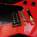Detail červené elektrické kytary s černým plechtrátem. Nástroj má dva humbuckery se zlatými ladicími šroubky, zlatý most a zlatý stop-bar strunovník.…