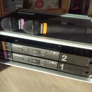 Černý přepravní kufr s polstřováním obsahuje dva bezdrátové mikrofony a dvě přijímačky. Na mikrofonech i přijímačkách je nápis audio-technica a AT-ON…