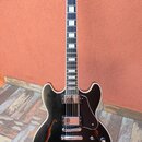 Černá polodupatá elektrická kytara s bílým lemováním a hnědým hmatníkem s blokovými vložkami. Na hlavě je bílý nápis Gibson. Nástroj má dva humbucker…