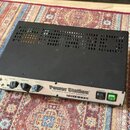 Černý kytarový zesilovač v kovovém šasi s ventilačními otvory na horní straně. Na předním panelu je nápis Power Station, Integrated Reactance Amplifi…