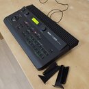 Černý tónový generátor s nápisem YAMAHA TG33 (TONE GENERATOR). Zařízení má digitální displej, několik tlačítek a jeden otočný ovladač. Vedle přístroj…