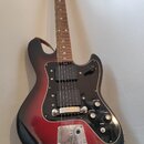 Elektrická kytara s trupem v červeno-černém přechodovém lakování a černým pickguardem. Na hlavě hmatníku je viditelné logo Squier. Nástroj má jeden v…