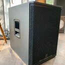 Černý subwoofer v hranatém korpusu s texturovaným povrchem a kovovou voštinovou mřížkou. Na boku je umístena integrovaná plastová rukojeť pro přenos.…
