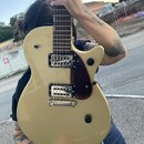 Elektrická kytara s jednobarvou zlatou povrchovou úpravou korpusu a hnědým hmatníkem. Nástroj má dva humbuckery s kovovými kryty, tmavě hnědý pickgua…