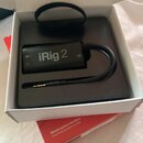 Černý kytarový interface iRig 2 v originální krabici. Na zařízení je bílý nápis „iRig 2“ a symboly pro zapnutí a výstup. K zařízení vede kabel zakonč…
