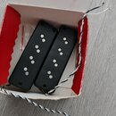 Dvě černé elektrické snímače typu humbucker v bílo-červeném papírovém krabičce. Snímače mají plastové kryty s viditelnými bílými póly. Z nástrojů ved…