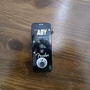 Černý efekt pedál s kovovým povrchem a bílým nápisem ABY. Na zařízení jsou viditelné texty DC IN, MICRO, CHANNEL SWITCH A/B, Y(A&B) a instrukce A:RED…