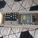 Fotografie zachycuje otevřený dřevěný box, ve kterém je umístěn černý elektronický modul s ovládacími knoflíky a přepínači. Na modulu je nápis bohm o…