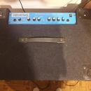 Modrý basový kombo zesilovač s černým textilním potahem skříně. Na horním ovládacím panelu je nápis NEMESIS a text 200 Watt Bass Guitar Combo Amplifi…