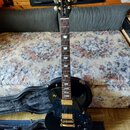 Černá elektrická kytara typu Les Paul s gold hardwarem a hnededým hmatníkem. Na hlavě je vidět nápis "Les Paul Custom" a logo "Alvarez". Nástroj je u…