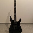 Černá elektrická kytara s černým povrchem a tmavým hmatníkem. Na hlavě je viditelné logo Jackson. Nástroj má dva humbuckery a dvě ovládací knoflíky,…