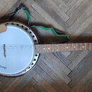 Bílý banjo s hnědým dřevěným krkem a tmavě hnědým korpusem. Na bílé membráně je v dolní části nápis Mustang. Nástroj má připevněný světlý dřevěný opě…