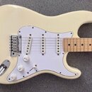 Krémově bílá elektrická kytara typu Stratocaster s bílým pickguardem a hnedým javorovým hmatníkem. Nástroj má tři bílé snímače, chromovaný most a tři…