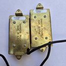 Dvě elektrické snímače s kovovými kryty zlaté barvy. Na obou je vyražen nápis DIMARZIO PICKUPS MADE IN U.S.A. a přilepeny bílé štítky s označením DP1…