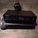 Černý bezdrátový přijímač s nápisem MALONE WIRELESS RECEIVER, vybavený dvěma ovladači hlasitosti VOL+ a VOL- a kontrolkami RF. Před přijímačem leží d…