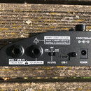 Zadní strana černého elektronického zařízení s texty a ovládacími prvky. Jsou zde dva velké konektory s nápisy INST. / LINE IN FROM AMP a TO SPEAKER,…