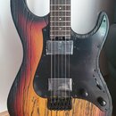 Elektrická kytara s tělem v přechodové barvě od černé přes červenou po žlutou s výraznou strukturou dřeva. Nástroj má černý pickguard, dva snímače s…
