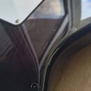 Detailní záběr na černý lakovaný povrch elektrokitary s kovovým krytem snímače. Na lakovaném povrchu jsou vidět drobné škrábance a dvě výraznější odl…