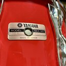 Detail červeného korpusu bubnu s kovovým štítkem. Na štítku je logo a nápis YAMAHA, dále údaje MODEL SD098, SER. NO. NY5979 a nápis MADE IN JAPAN. Po…