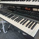 Černý digitální syntezátor s klávesnicí, na jehož ovládacím panelu je vlevo nápis DX7ii. Přístroj obsahuje množství tlačítek, posuvníků a textových p…