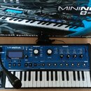 Modrý kompaktní syntetizátor s klávesnicí a černým šasi. Na přístroji je nápis MININOVA synthesizer a logo novation. Nad klávesnicí se nachází disple…