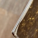 Detailní záběr na roh předmětu s hnědou, texturovanou povrchovou vrstvou a stříbrným kovovým okrajem. V místě ohnutí rohové hrany je viditelné odslou…