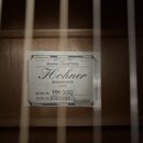 Fotografie zachycuje štítek uvnitř akustického nástroje. Na bílém štítku je uveden nápis HAND CRAFTED, značka Hohner a text Established 1857. Je zde…