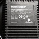 Černý plastový napájecí adaptér s žebrovaným povrchem. Na štítku je uveden název BEHRINGER a model EURORACK POWER SUPPLY MODEL MXEU1 CLASS 2 TRANSFOR…