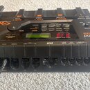 Černý kytarový procesor Roland GR-33 s digitálním displejem a řadou ovládacích tlačítek. Na horní části jsou nápisy BANK, HOLD, P-GLIDE a WAH, vpravo…