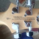 Záběr na zadní stranu hlavy kytary z přírodního světlého dřeva s chromovanými ladicími kolíky. Na dřevě je černý nápis: Built by Cor-Tek Musical Inst…