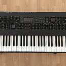 Černý klávesový syntetizátor s bílými a černými klávesami. Na levé straně horního panelu je bílý nápis SEQUENTIAL PROPHET XL a vpravo nápis 8DIO. Pře…