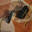 Fotografie zachycuje dva snímače k elektrické kytáře s připojenými vodiči. Jeden snímač je v chromovém krytu, druhý je černý s viditelnými póly. Na s…