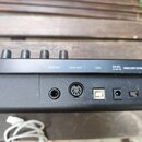 Detail zadní strany černého elektronického nástroje s řadou konektorů. Jsou zde nápisy SUSTAIN, MIDI OUT, USB a 5V DC s označením USB | OFF | POWER.…