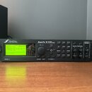 Černý rackový procesor s nápisy FRACTAL AUDIO SYSTEMS a Axe-Fx II PREAMP/FX PROCESSOR. Zařízení má digitální displej s zeleným podsvícením, několik o…