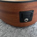 Detailní pohled na bok dřevěné akustické kytary v hnědé barvě s černým lemováním. Na boku je umístěn černý plastový panel s nápisem FISHMAN a konekto…