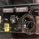 Černý pedálboard s několika efekty a dvěma zdroji napájení s nápisy MULTI POWER SUPPLY, SEPARATE ISOLATED 8X DC10V / 100mA a SMRCKAEFFECTS. Na desce…