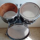 Tři černé bubny s kovovými obručemi. Na bílých kožích jsou viditelná loga Mapex a Sonor. Jeden z bubnů je zobrazen bez horní kože, je vidět dřevěný v…