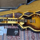 Polodupatá elektrická kytara s trupem v barevnosti sunburst uložená v černém tvrdém kufru s žlutým vnitřkem. Na hlavě hmatníku je bílý nápis Gibson a…