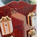 Detail hlavy červené kytary s viditelným sériovým číslem 215240033. Na povrchu je nápis MADE IN USA a jsou vidět tři strojky s nápisy GIBSON DELUXE.…