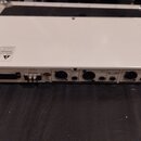 Zadní strana bílého elektronického zařízení s řadou konektorů. Jsou zde vidět nápisy OUTPUT a INPUT u několika zapadacích konektorů, dále varovný ští…