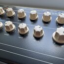 Černý elektronický přístroj s řadou bílých plastových oválových ovladačů. Na horní hraně jsou nápisy 12 VDC, OVERALL, GATE, SWITCH, AUDIO, MIDI IN, M…