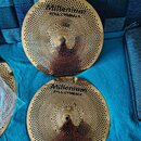Dvě zlaté kovové činely s perforací v podobě malých otvorů po celém povrchu. Na obou je vyražen nápis Millenium STEEL CYMBALS. Činely jsou v novém st…