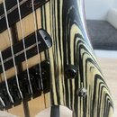 Detail korpusu basové kytary s výraznou žlutobílou sletovanou dřevěnou strukturou a černými pruhy. Nástroj má černé hardware, včetně dvou snímačů a m…