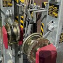 Fotografie znázorňuje detail kovové konstrukce s mechanismy kladkových kol a ocelovými lany. Na žlutých štítcích je uveden text T-106 ELEVATOR TOWER…