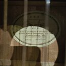Fotografie zachycuje vnitřní štítek akustické kytary přilepený k dřevěné desce. Na štítku je logo Fender, model CN90 NAT a text Made in accordance to…